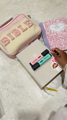 a person is writing on a notebook next to a pink and white bag with personalized items