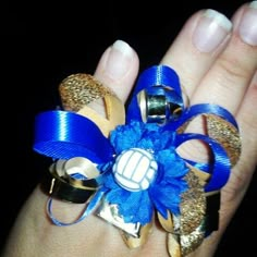 a woman's hand with blue and gold hair accessories on her ring, which is decorated with an image of a volleyball ball