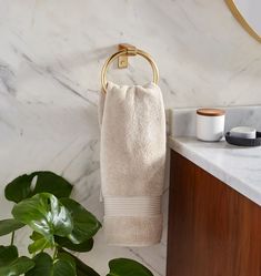 a white towel hanging on a gold ring in a bathroom with marble counter top and wooden cabinet