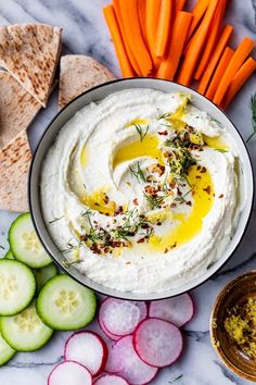 a bowl of hummus, carrots, cucumbers and crackers