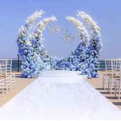 an outdoor wedding setup with blue and white flowers on the aisle, chandelier and chairs