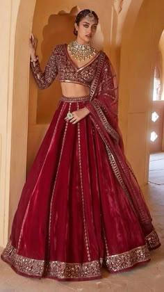 a woman in a red lehenga standing by a wall with her hand on her hip