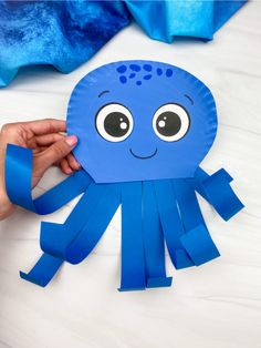 a paper plate octopus craft is being held up by someone's hand with scissors