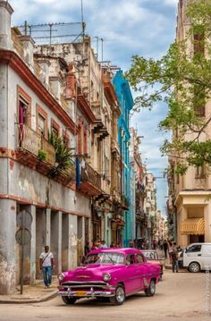 an old pink car is parked on the side of the road in front of some buildings