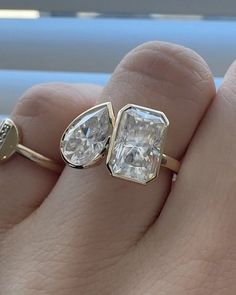 a woman's hand holding two engagement rings in front of her face and the other side with an oval shaped diamond on it