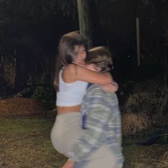 two young women hugging each other in the middle of a yard at night with trees and bushes behind them