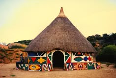 a thatched hut with colorful designs painted on the side and a woman standing in front