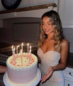 a woman holding a cake with lit candles on it in front of a counter top