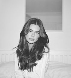 a black and white photo of a woman sitting on a bed with her hair blowing in the wind