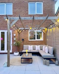 an outdoor living area with couches, tables and lights on the side of a brick building