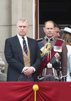 two men in suits and ties standing next to each other on the balcony of buckingham palace