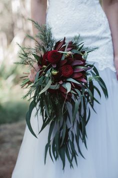 a bride holding a bouquet of red flowers and greenery