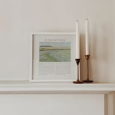 two candles are sitting on a mantle next to a framed photograph and a candle holder