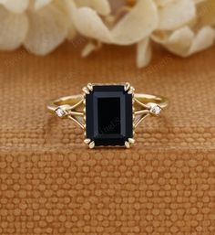 a black stone ring sitting on top of a wooden table next to white flower petals