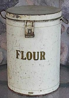 an old white bucket with the word flour on it sitting in front of a stone wall