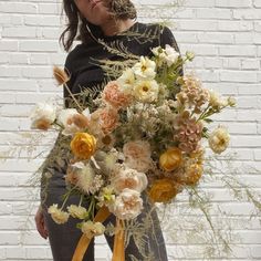 a woman holding a bouquet of flowers in front of a white brick wall with yellow ribbon