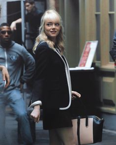 a woman is walking down the street carrying a black handbag in her right hand