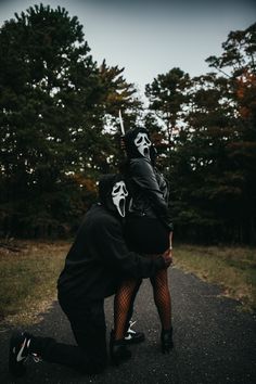 two people in black outfits and white masks on their faces, one is holding the other's head