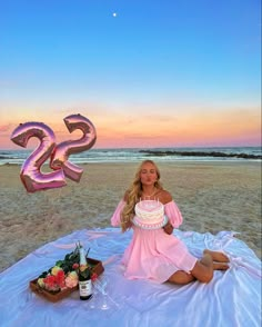 a woman sitting on top of a blanket holding a cake in front of the ocean