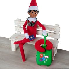 an elf is sitting on a bench next to a green suitcase with a camera in it