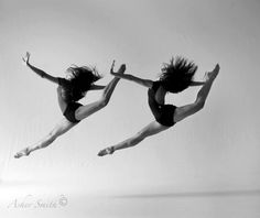 two women are jumping in the air with their legs spread out and one is wearing a leotard