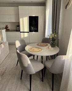 a white table with four chairs around it in the middle of a living room and kitchen area