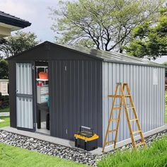 a small gray shed with a ladder next to it on the grass and trees in the background