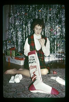 a woman sitting on the floor next to a christmas tree with stockings around her ankles