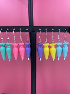 several different colored vases hanging from hooks on a pink wall with earrings attached to them