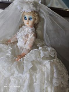 a doll dressed in a white wedding dress and veil sitting on a bed with her head down