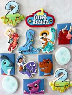 some cookies that are decorated to look like dinosaurs and dino ranch characters on top of each other