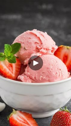 two scoops of strawberry ice cream in a bowl with strawberries on the side