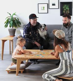 three adults and two children sitting on a couch playing board games with a dog in the background