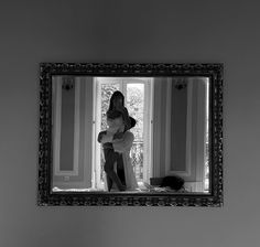 a woman standing in front of a mirror with her reflection on the wall behind her