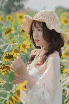 a woman standing in a field of sunflowers wearing a white dress and hat