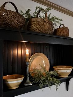 a shelf with plates and baskets on top of it next to a lit candle in the corner