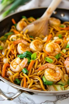 a wok filled with noodles and shrimp on top of a marble counter next to chopsticks