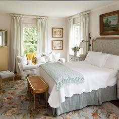 a bed sitting in a bedroom next to a window covered in white sheets and pillows