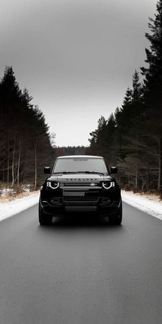 a black car is driving down the road in front of some pine trees and snow