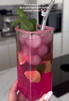 a hand holding a glass filled with pink liquid and green leafy garnish