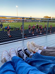 people are sitting on the bleachers at a football game with their feet propped up