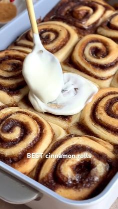 cinnamon rolls with icing being drizzled on top in a baking dish