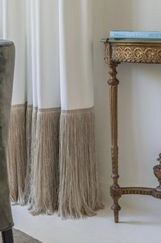 a table with a book on top of it next to some curtains and a vase