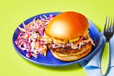 a blue plate topped with a burger and coleslaw slaw next to a fork