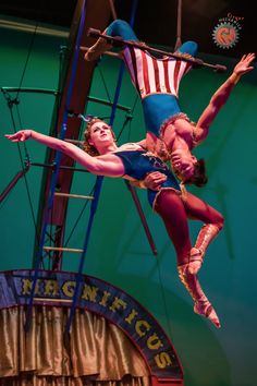 two circus performers performing aerial tricks on the rings in front of an american flag banner