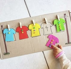 a child's hand is pointing at clothes hanging on a line with pegs