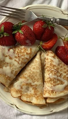 some pancakes with strawberries on a plate next to a fork and knife, sitting on a white table cloth