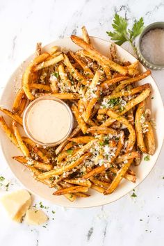 french fries with parmesan cheese and sauce on a white plate next to garlic