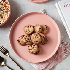 chocolate chip cookies on a pink plate next to a book