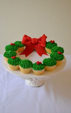 cupcakes with green frosting and red bows are on a white cake plate